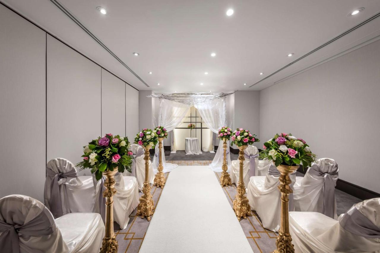 Radisson Blu Plaza Hotel Sydney Eksteriør billede The photo shows a beautifully arranged indoor event space, likely set up for a wedding ceremony. There is a long white aisle runner leading to a decorated archway at the end. On either side of the aisle, there are elegant chairs draped in white fabri