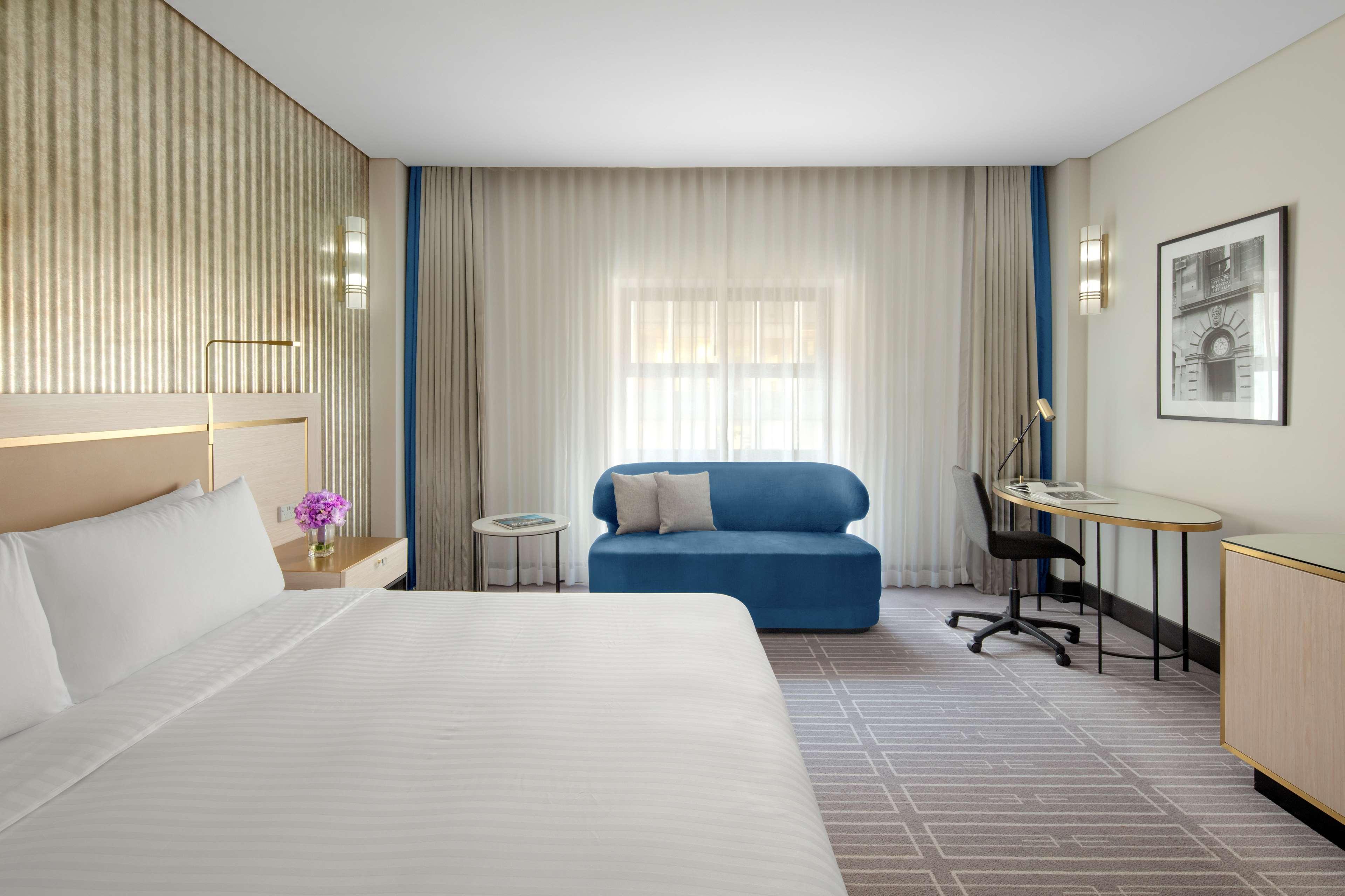 Radisson Blu Plaza Hotel Sydney Eksteriør billede The photo shows a modern hotel room featuring a large bed with white linens. There's a small table with a flower vase next to the bed. A blue sofa is positioned against one wall, and a desk with a chair is situated nearby. The room has soft, diffused