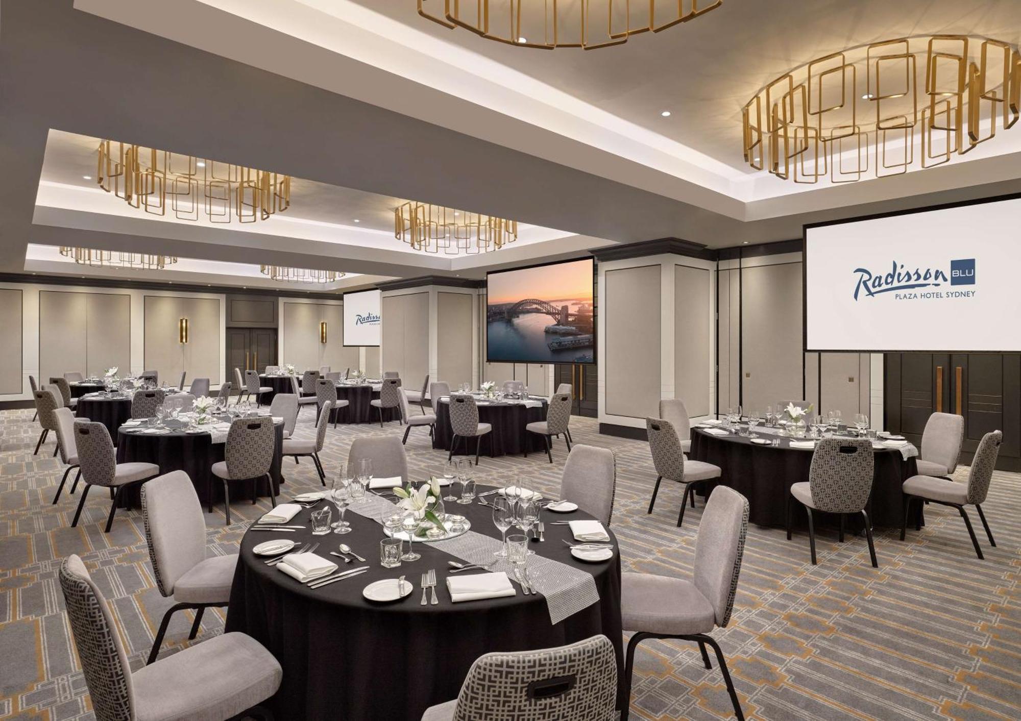 Radisson Blu Plaza Hotel Sydney Eksteriør billede The photo shows an elegant banquet or conference room setup at a Radisson hotel. The space features multiple round tables, each adorned with white tablecloths, centerpieces, and plates, ready for dining. The room is well-lit, highlighting modern deco