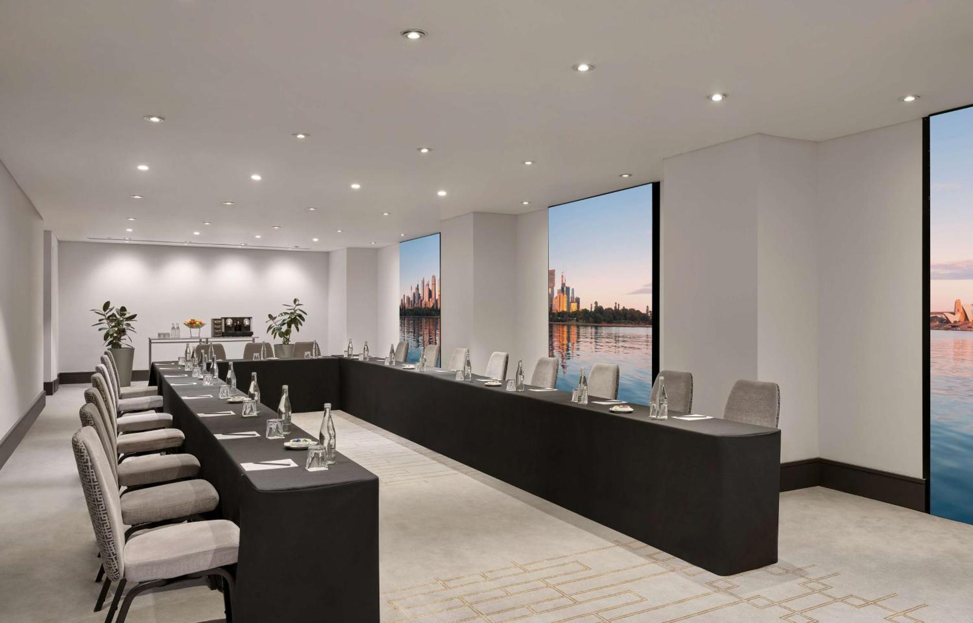 Radisson Blu Plaza Hotel Sydney Eksteriør billede The photo depicts a modern conference room set up for a meeting. The room features a long, rectangular table with multiple chairs arranged along its sides. Each chair is equipped with items such as water bottles and notepads. Large windows allow natu